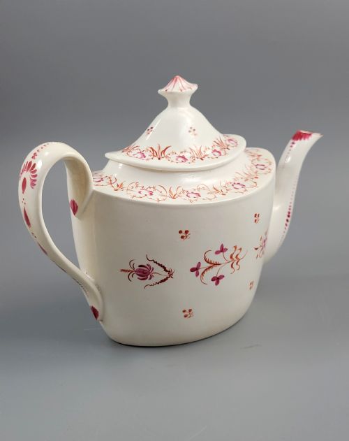 fig 2. A cream-coloured Georgian porcelain teapot decorated with hand-painted reddish-pink floral sprigs, featuring a high lid with a knop and a curved spout.