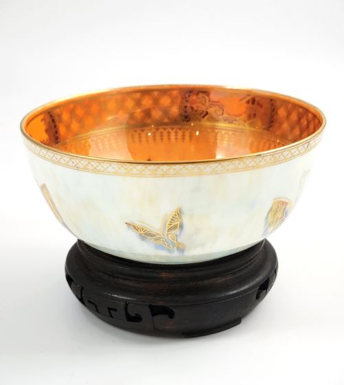 fig 1. A rounded ceramic lustreware bowl featuring polychrome butterfly illustrations on an iridescent white exterior and an orange gilded interior.