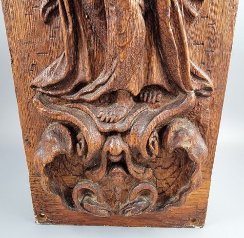 fig 4. A vertical carved oak panel displaying a high-relief figure of Faith holding a cross and a book beneath ornate Baroque scrollwork.