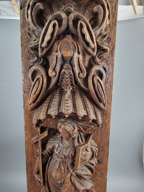 fig 3. A vertical carved oak panel displaying a high-relief figure of Faith holding a cross and a book beneath ornate Baroque scrollwork.