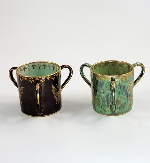 fig 1. A pair of small three-handled ceramic cups, one in deep purple with a gilded butterfly design and the other in iridescent green with a gilded snake motif.