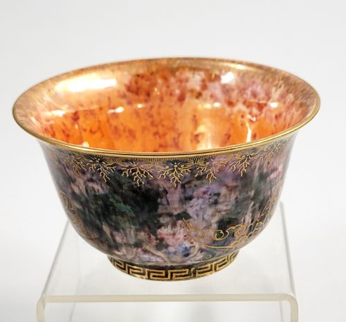 fig 2. A circular porcelain bowl featuring a mottled iridescent purple exterior decorated with gilt butterfly motifs and a gold-toned orange interior.