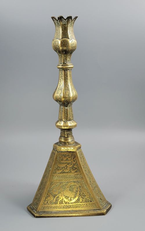 fig 1. A tall late 19th-century Qajar Persian brass candlestick featuring a wide triangular engraved base, a knopped stem, and a flared lotus socket.