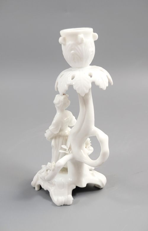 fig 1. An antique white glazed porcelain candlestick featuring a moulded figurine of a girl holding flowers atop a Rococo scroll base.