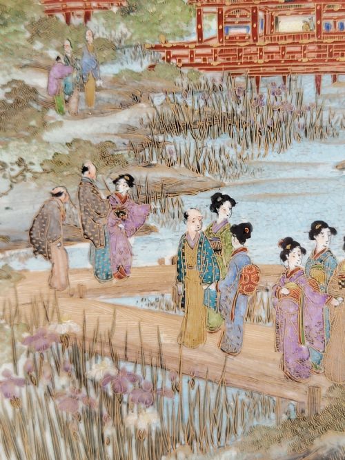 fig 3. A circular Meiji period Satsuma earthenware plate featuring finely detailed figures, temples, and wisteria framed by a gilt geometric border.