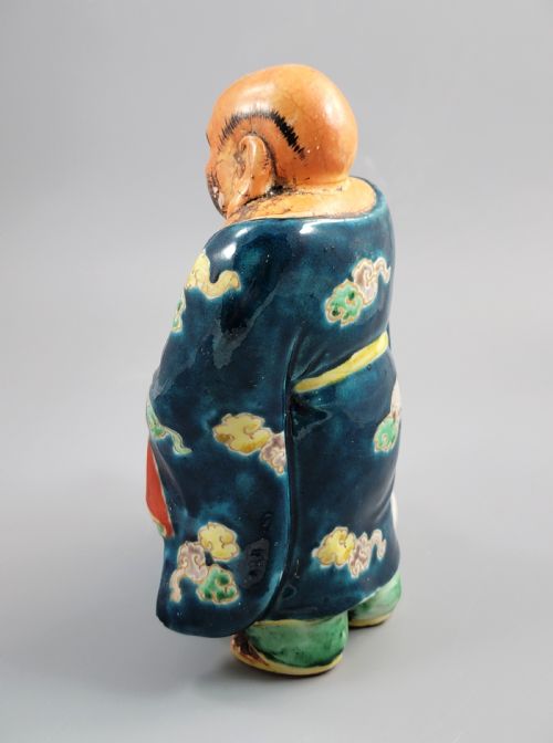 fig 2. A Japanese Satsuma earthenware figure depicting Hotei in patterned blue robes holding a fan, standing next to a small child on a patterned sack.