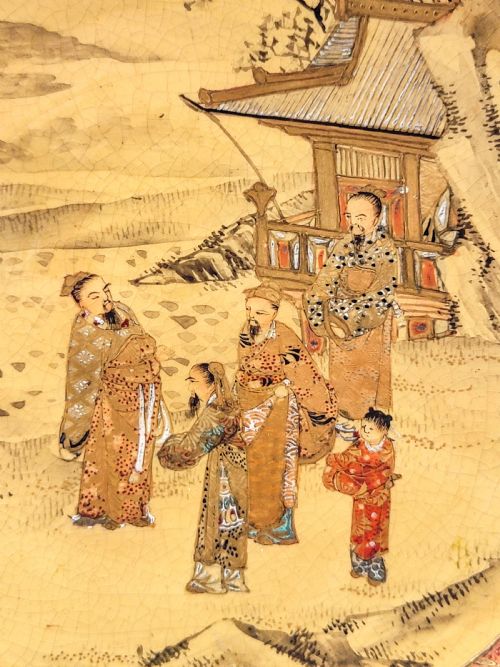 fig 1. A circular Japanese Satsuma earthenware plate featuring a fine crackle glaze, detailed polychrome figures in traditional dress near a landscape building, and a gilded geometric border.