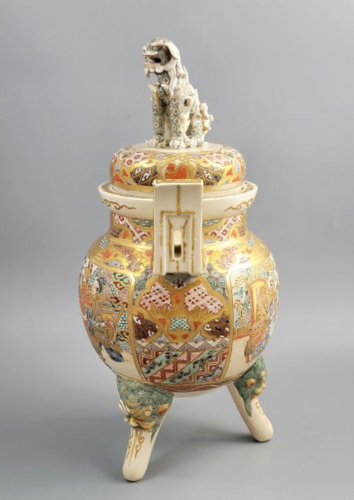 fig 2. A cream-coloured Japanese Satsuma earthenware incense burner featuring a lid with a shishi lion finial, upright handles, tripod feet, and detailed polychrome paintings of samurai warriors with gold accents.