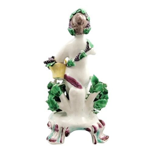 fig 2. An 18th-century Bow soft-paste porcelain figure of a putto adorned with grapevines, standing on a Rococo scroll base with colourful floral bocage behind.