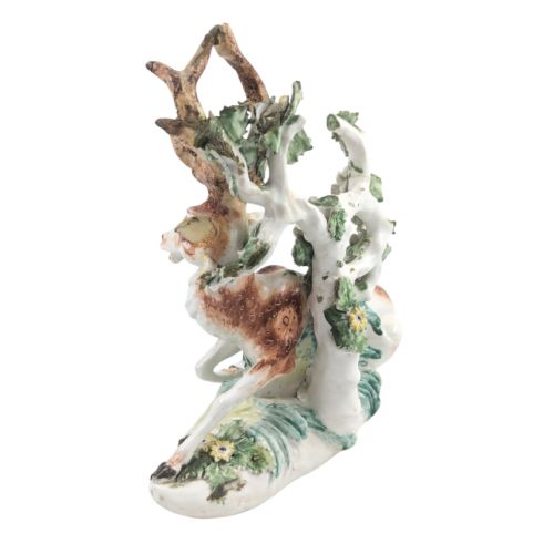 fig 2. An 18th-century soft-paste porcelain figurine depicting a recumbent brown and white spotted stag resting in front of a leafy bocage with small yellow flowers.