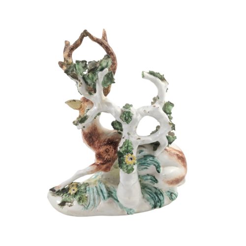 fig 4. An 18th-century soft-paste porcelain figurine depicting a recumbent brown and white spotted stag resting in front of a leafy bocage with small yellow flowers.