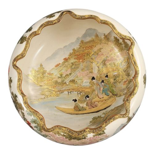 fig 1. A Japanese Satsuma earthenware bowl with hand-painted figures under trees and gold accents, resting on a dark carved wooden stand.