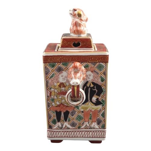 fig 1. A rectangular Japanese porcelain incense burner featuring hand-painted depictions of a European ship, decorative red enamel borders, animal head handles, and a shishi lion finial on the lid.