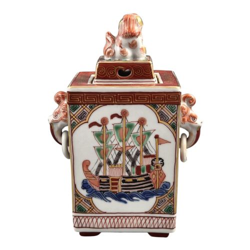 fig 2. A rectangular Japanese porcelain incense burner featuring hand-painted depictions of a European ship, decorative red enamel borders, animal head handles, and a shishi lion finial on the lid.