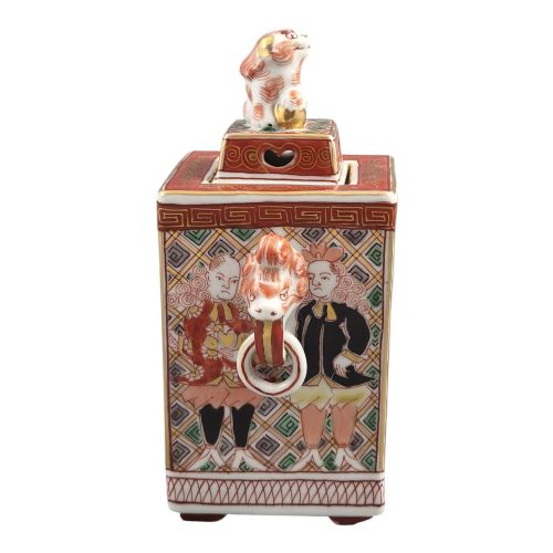fig 3. A rectangular Japanese porcelain incense burner featuring hand-painted depictions of a European ship, decorative red enamel borders, animal head handles, and a shishi lion finial on the lid.