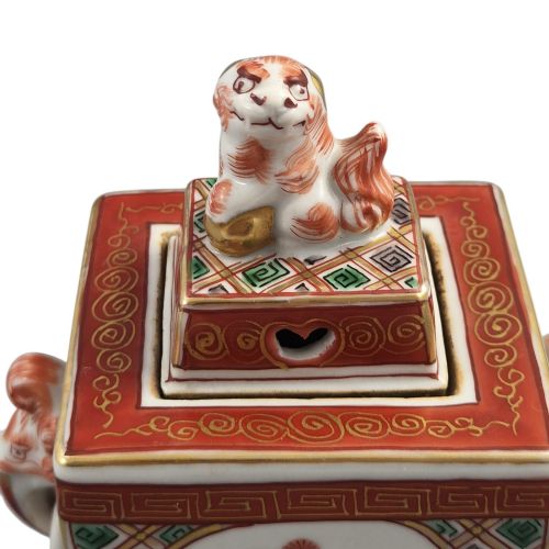 fig 4. A rectangular Japanese porcelain incense burner featuring hand-painted depictions of a European ship, decorative red enamel borders, animal head handles, and a shishi lion finial on the lid.