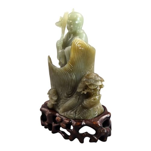 fig 1. A carved pale green Chinese jadeite figure holding a lotus stem, resting on a fitted dark carved wooden stand.