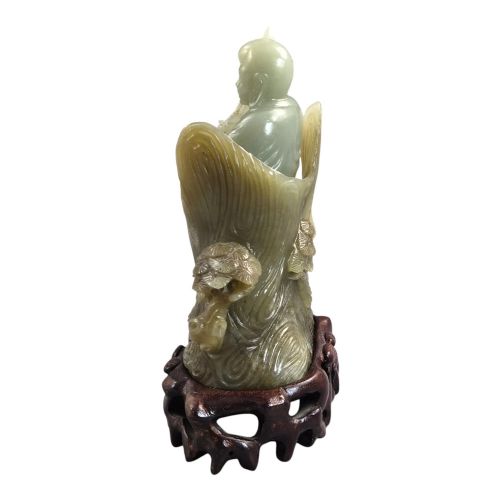fig 2. A carved pale green Chinese jadeite figure holding a lotus stem, resting on a fitted dark carved wooden stand.