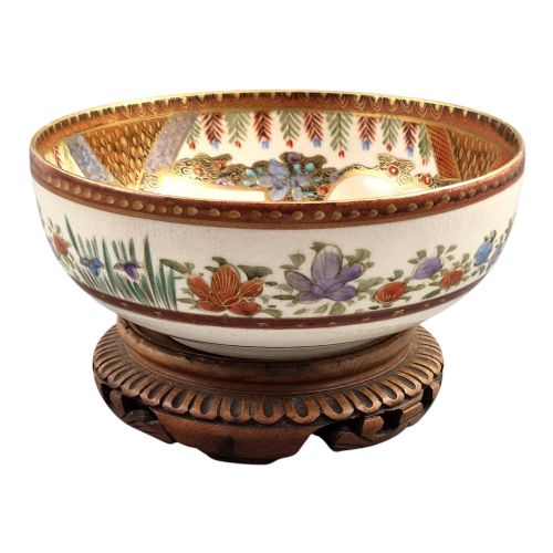 fig 2. An antique Meiji period Japanese Satsuma earthenware bowl featuring hand-painted floral panels and gold detailing, elevated on a carved dark wooden base.