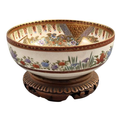 fig 3. An antique Meiji period Japanese Satsuma earthenware bowl featuring hand-painted floral panels and gold detailing, elevated on a carved dark wooden base.