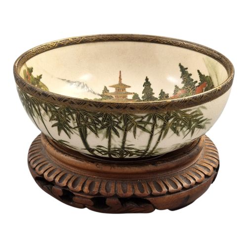 fig 5. An antique cream earthenware bowl resting on a carved wooden base, decorated inside with hand-painted Japanese landscapes and figures, and finished with a bamboo pattern around the exterior.