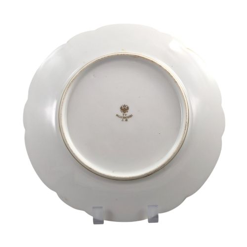 fig 4. A white round porcelain plate featuring a thick cobalt blue scalloped border and a gilded Imperial monogram topped with a crown.