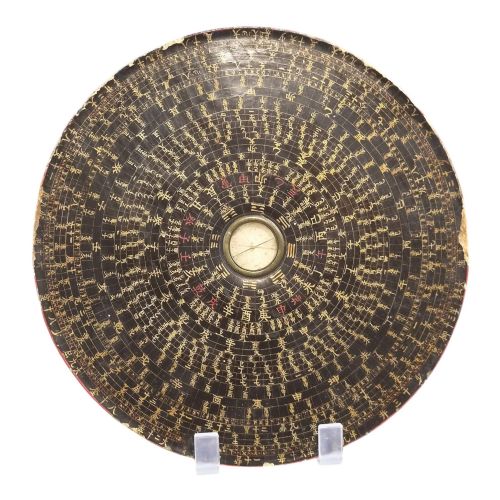 fig 1. A circular antique Chinese Luopan geomantic compass crafted from dark lacquered wood featuring multiple concentric rings of gilded Chinese characters and a central brass magnetic dial.