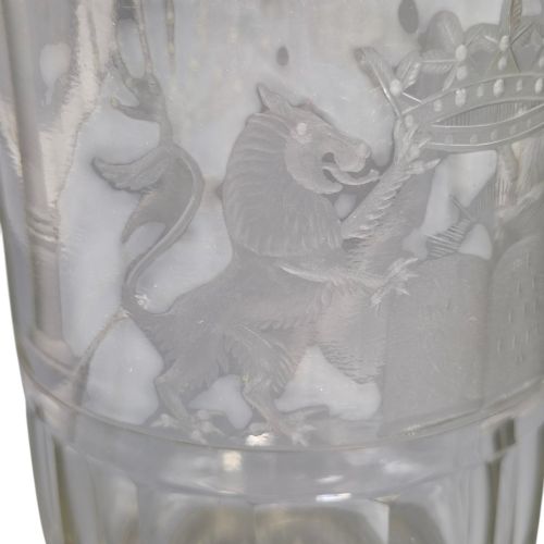 fig 7. A large clear glass beaker featuring detailed wheel-engraved ceremonial iconography, vertical fluted panels near the lower rim, and a faceted base.