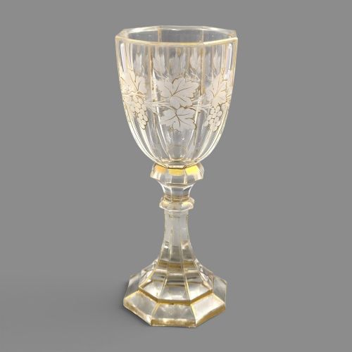 fig 3. A clear Bohemian crystal romer goblet featuring wheel-engraved grapevine motifs, a faceted stem, and gilt highlight accents on a hexagonal foot.