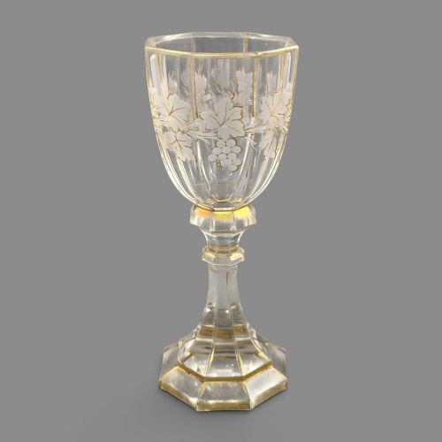 fig 4. A clear Bohemian crystal romer goblet featuring wheel-engraved grapevine motifs, a faceted stem, and gilt highlight accents on a hexagonal foot.