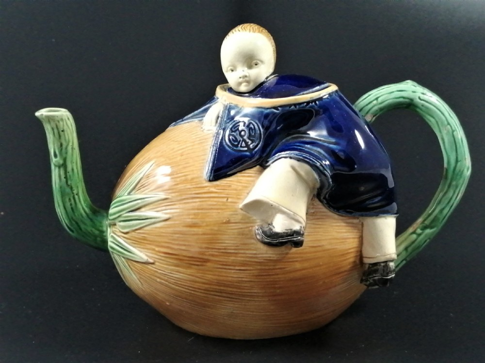 A Victorian earthenware majolica teapot shaped as a melon with a figure of a boy in a blue jacket seated on top forming the lid.