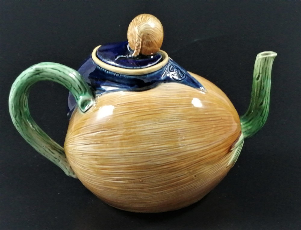 A Victorian earthenware majolica teapot shaped as a melon with a figure of a boy in a blue jacket seated on top forming the lid. View V