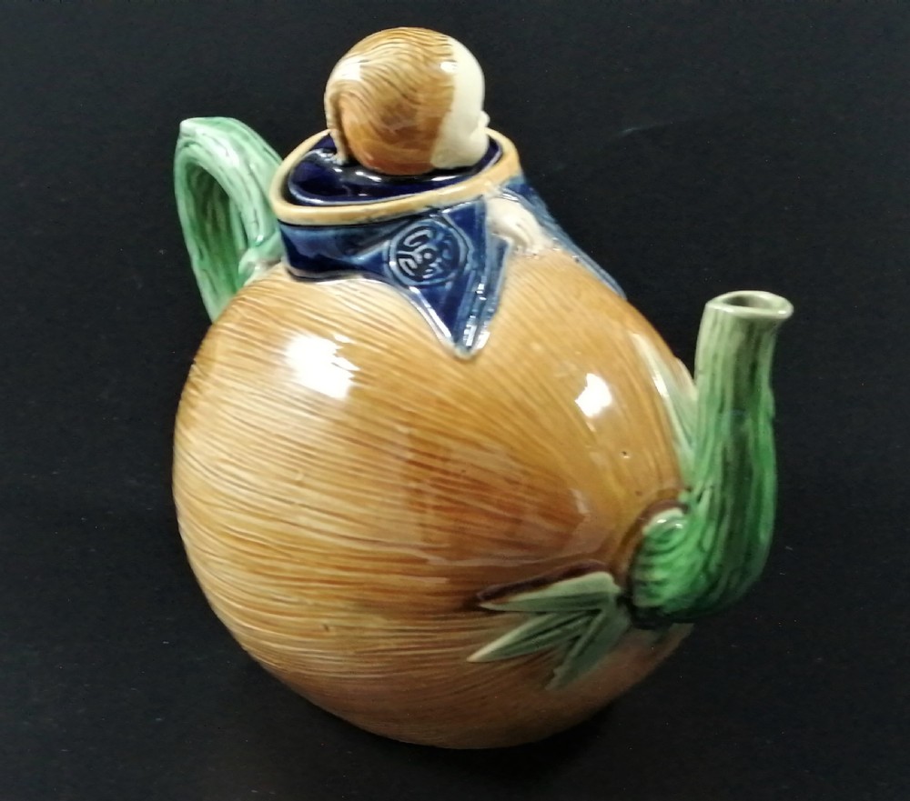 A Victorian earthenware majolica teapot shaped as a melon with a figure of a boy in a blue jacket seated on top forming the lid. View VI