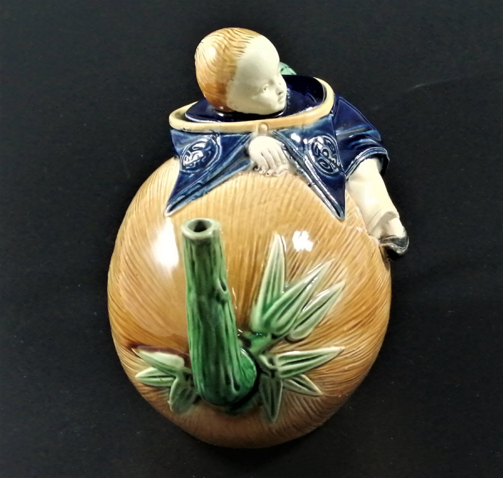 A Victorian earthenware majolica teapot shaped as a melon with a figure of a boy in a blue jacket seated on top forming the lid. View VII