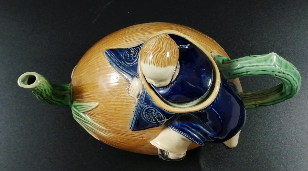 A Victorian earthenware majolica teapot shaped as a melon with a figure of a boy in a blue jacket seated on top forming the lid. View XI