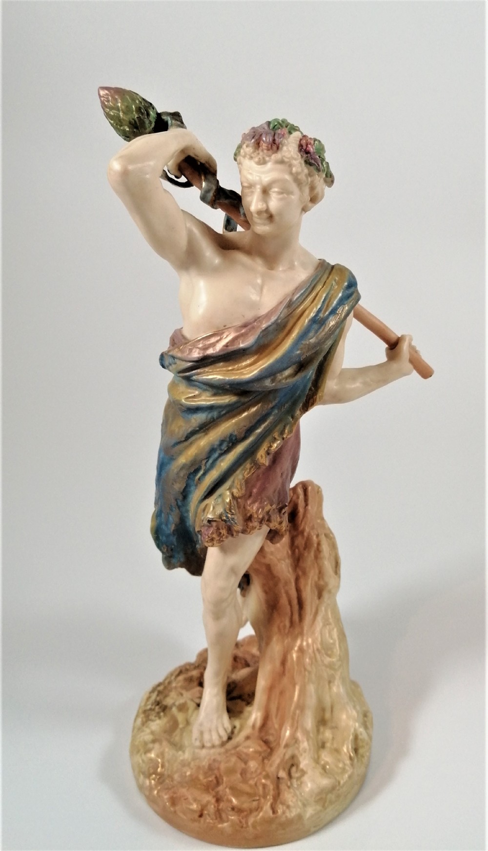 A Victorian Royal Worcester porcelain figurine depicting a male satyr draped in blue and gold robes, holding a staff over his shoulder.