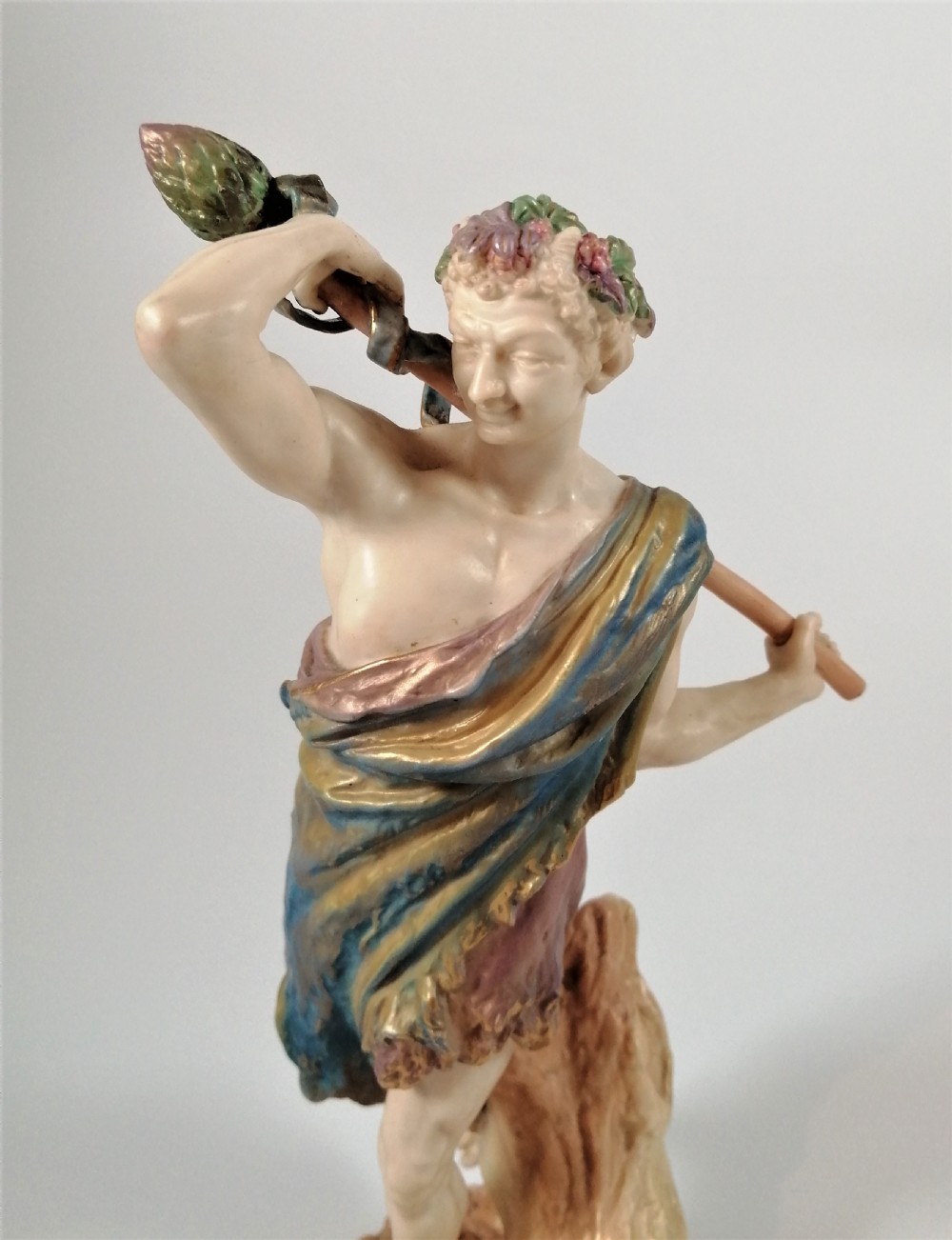 A Victorian Royal Worcester porcelain figurine depicting a male satyr draped in blue and gold robes, holding a staff over his shoulder. View II