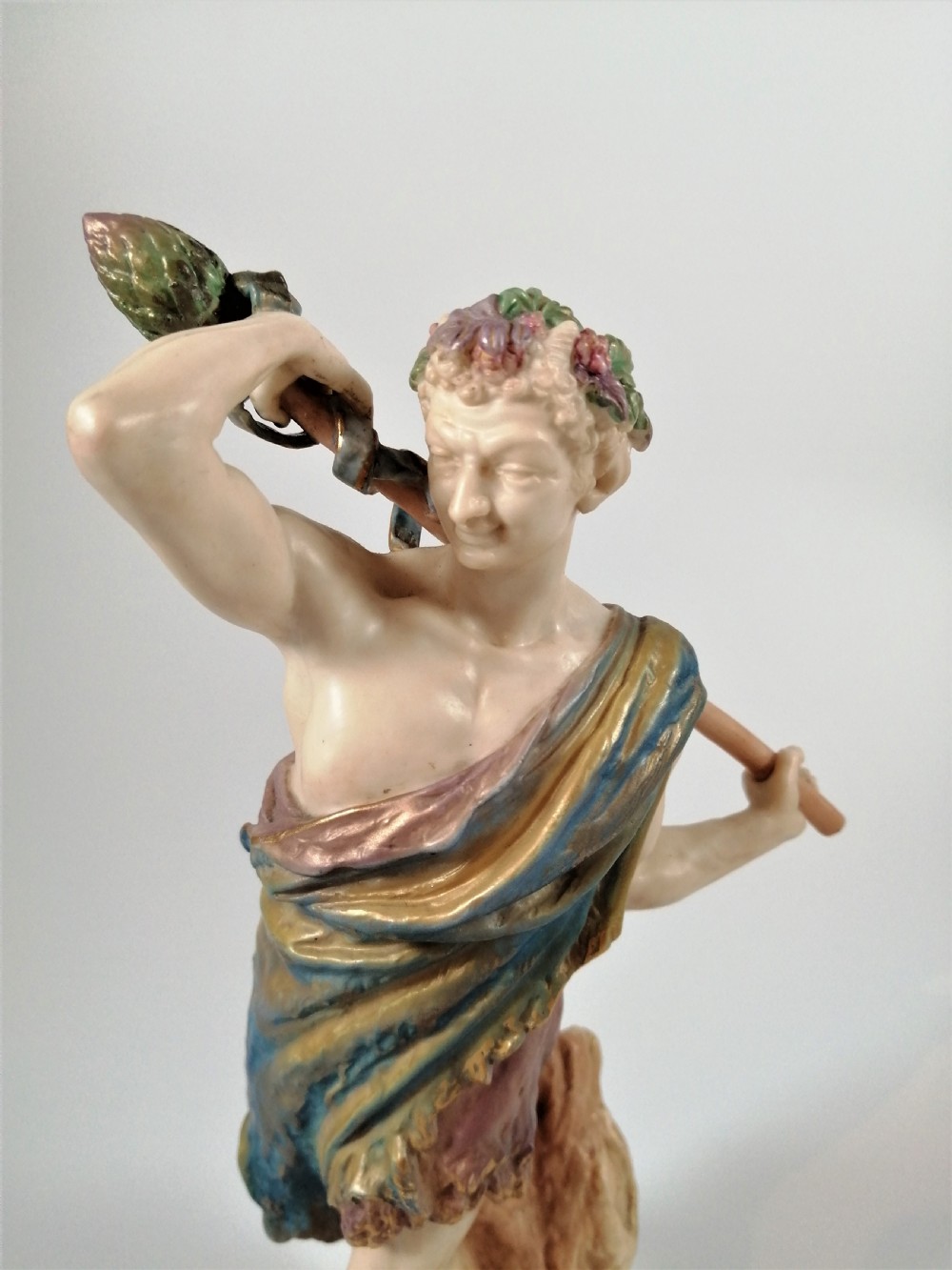 A Victorian Royal Worcester porcelain figurine depicting a male satyr draped in blue and gold robes, holding a staff over his shoulder. View III