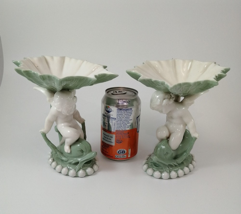 A pair of Victorian ceramic compotes featuring unglazed white cherub figures holding green leaf-shaped bowls aloft while seated on green glazed dolphin bases. View III