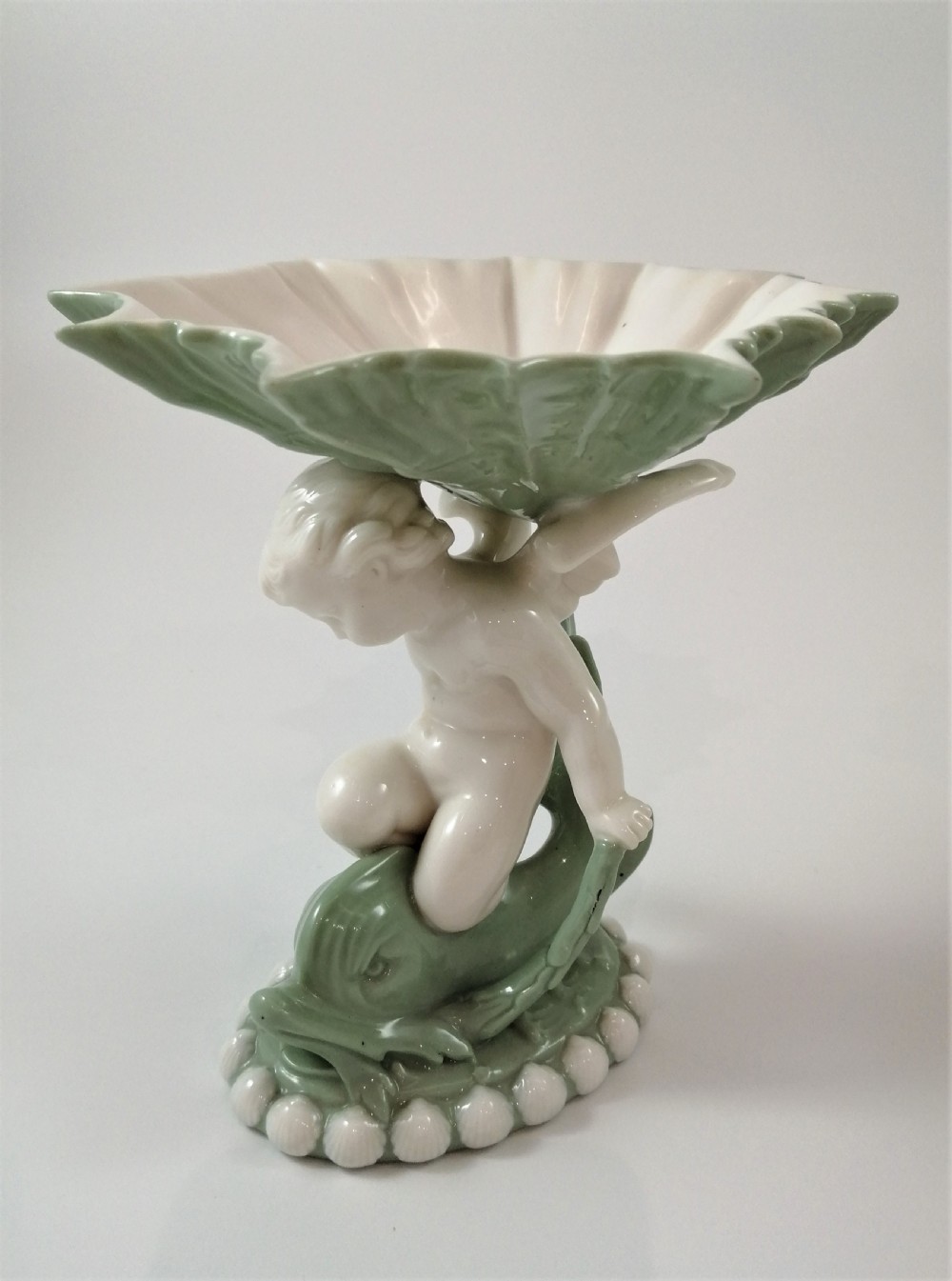 A pair of Victorian ceramic compotes featuring unglazed white cherub figures holding green leaf-shaped bowls aloft while seated on green glazed dolphin bases. View IV