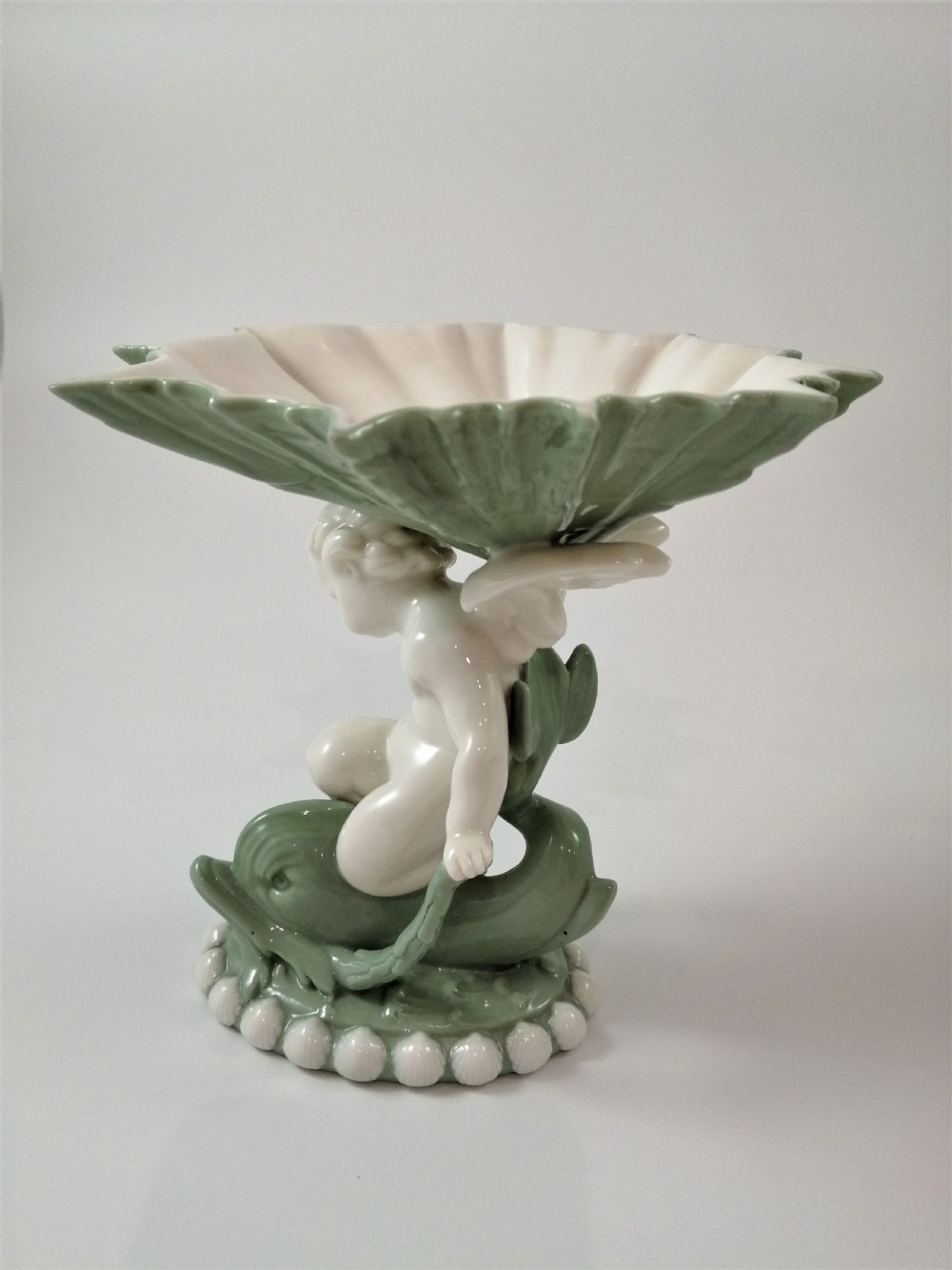 A pair of Victorian ceramic compotes featuring unglazed white cherub figures holding green leaf-shaped bowls aloft while seated on green glazed dolphin bases. View V