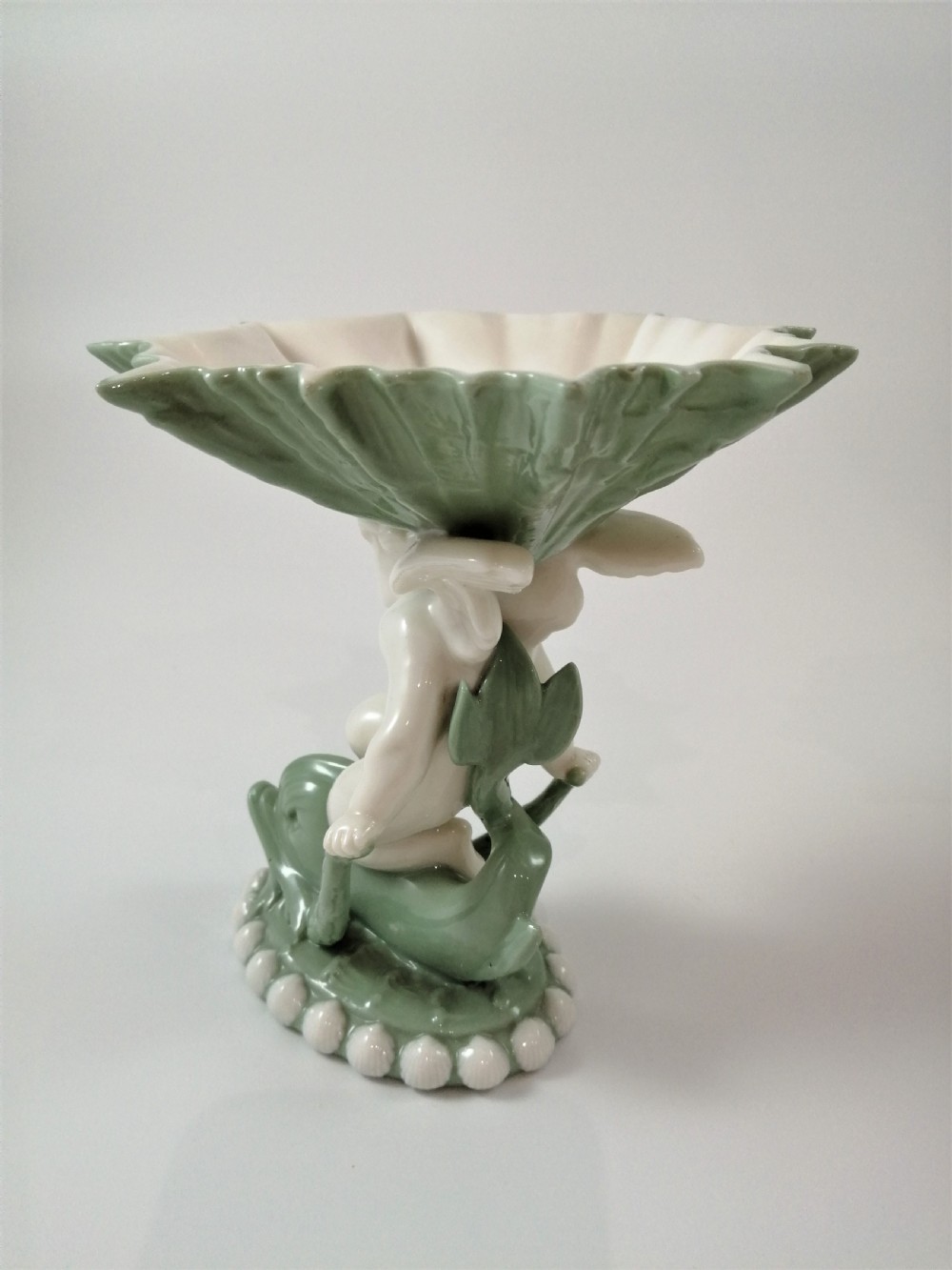 A pair of Victorian ceramic compotes featuring unglazed white cherub figures holding green leaf-shaped bowls aloft while seated on green glazed dolphin bases. View VI