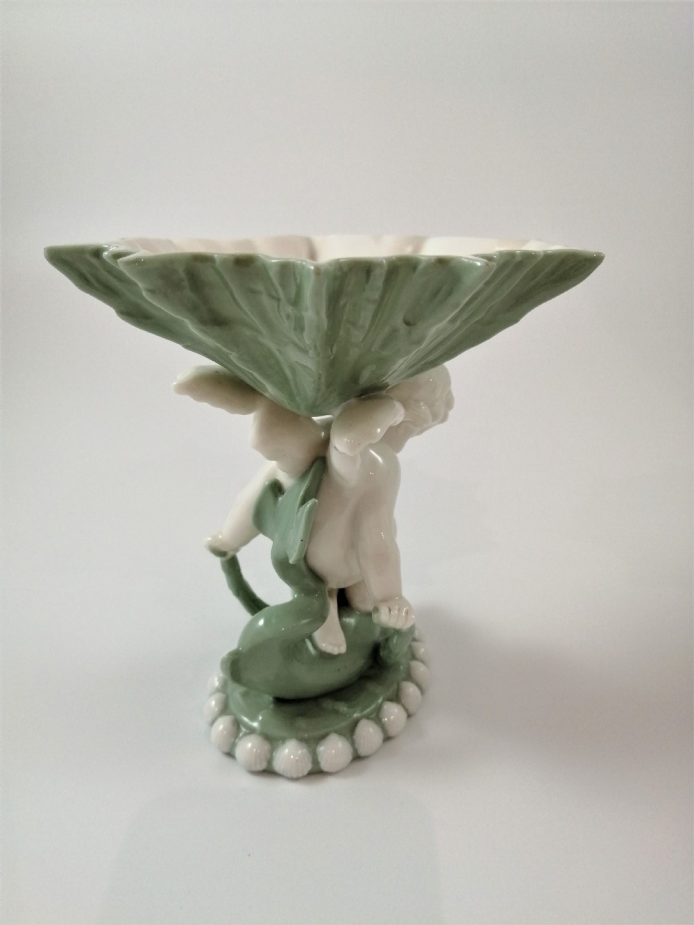 A pair of Victorian ceramic compotes featuring unglazed white cherub figures holding green leaf-shaped bowls aloft while seated on green glazed dolphin bases. View VII