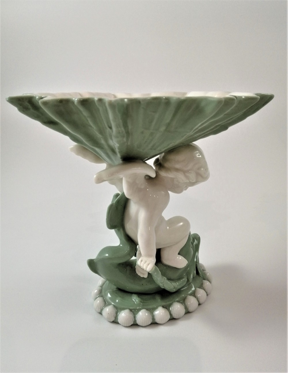 A pair of Victorian ceramic compotes featuring unglazed white cherub figures holding green leaf-shaped bowls aloft while seated on green glazed dolphin bases. View VIII