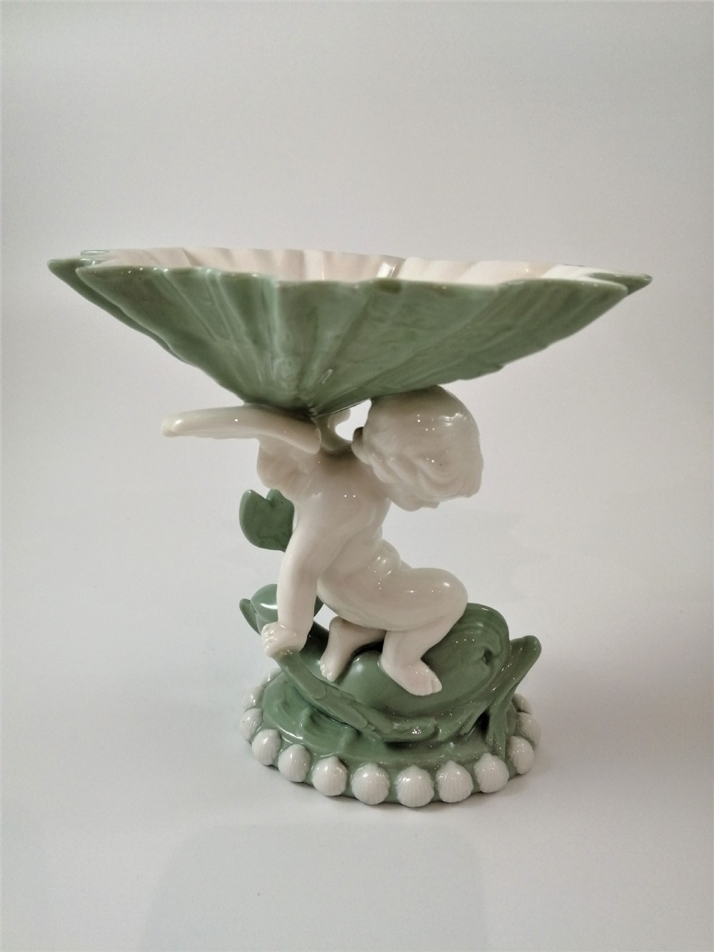 A pair of Victorian ceramic compotes featuring unglazed white cherub figures holding green leaf-shaped bowls aloft while seated on green glazed dolphin bases. View IX