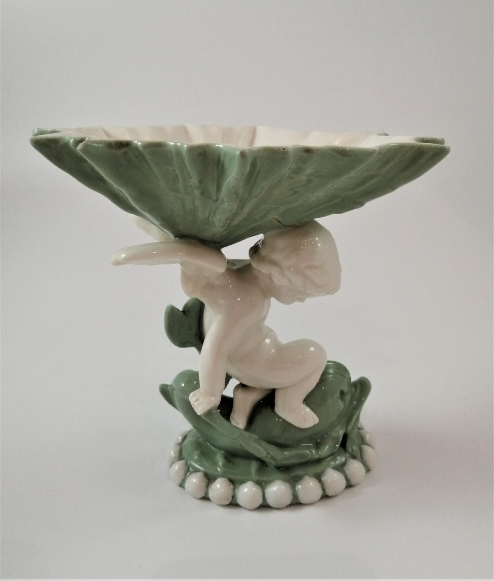 A pair of Victorian ceramic compotes featuring unglazed white cherub figures holding green leaf-shaped bowls aloft while seated on green glazed dolphin bases. View XI