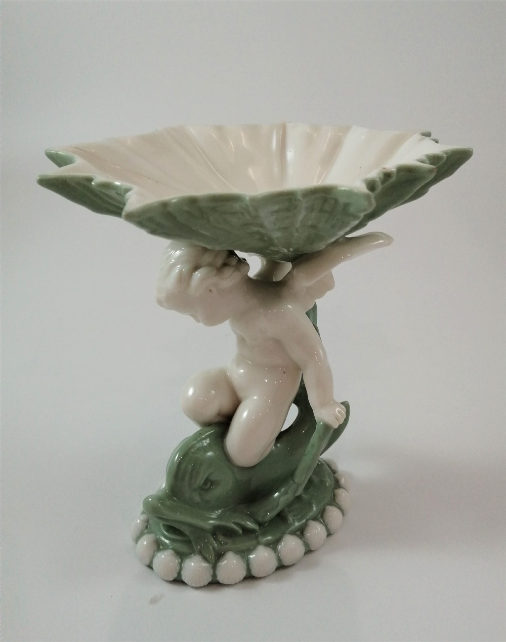A pair of Victorian ceramic compotes featuring unglazed white cherub figures holding green leaf-shaped bowls aloft while seated on green glazed dolphin bases. View XIII