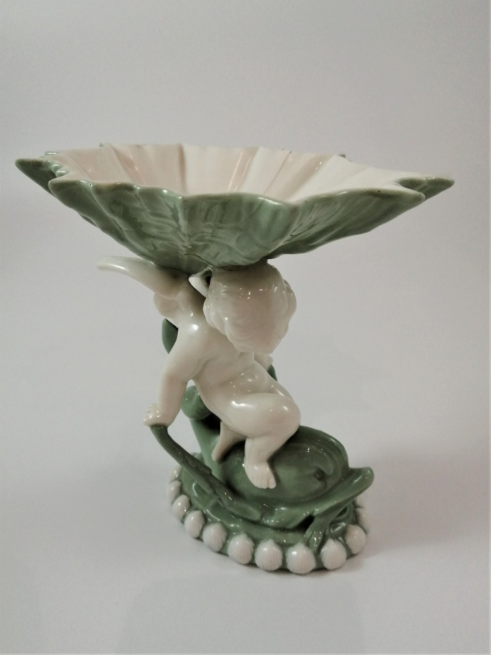 A pair of Victorian ceramic compotes featuring unglazed white cherub figures holding green leaf-shaped bowls aloft while seated on green glazed dolphin bases. View XV