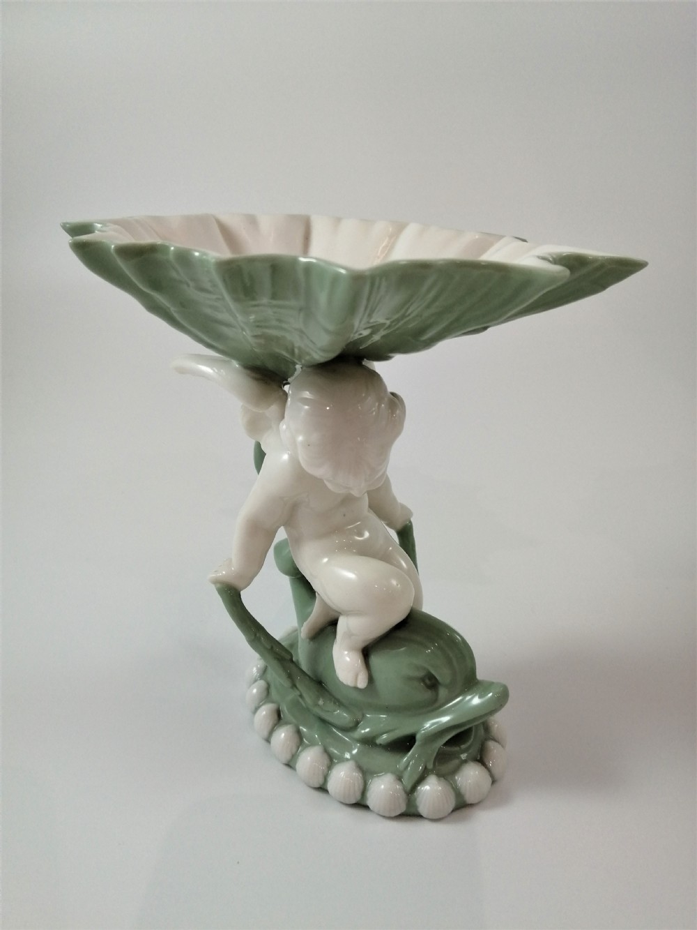 A pair of Victorian ceramic compotes featuring unglazed white cherub figures holding green leaf-shaped bowls aloft while seated on green glazed dolphin bases. View XIX