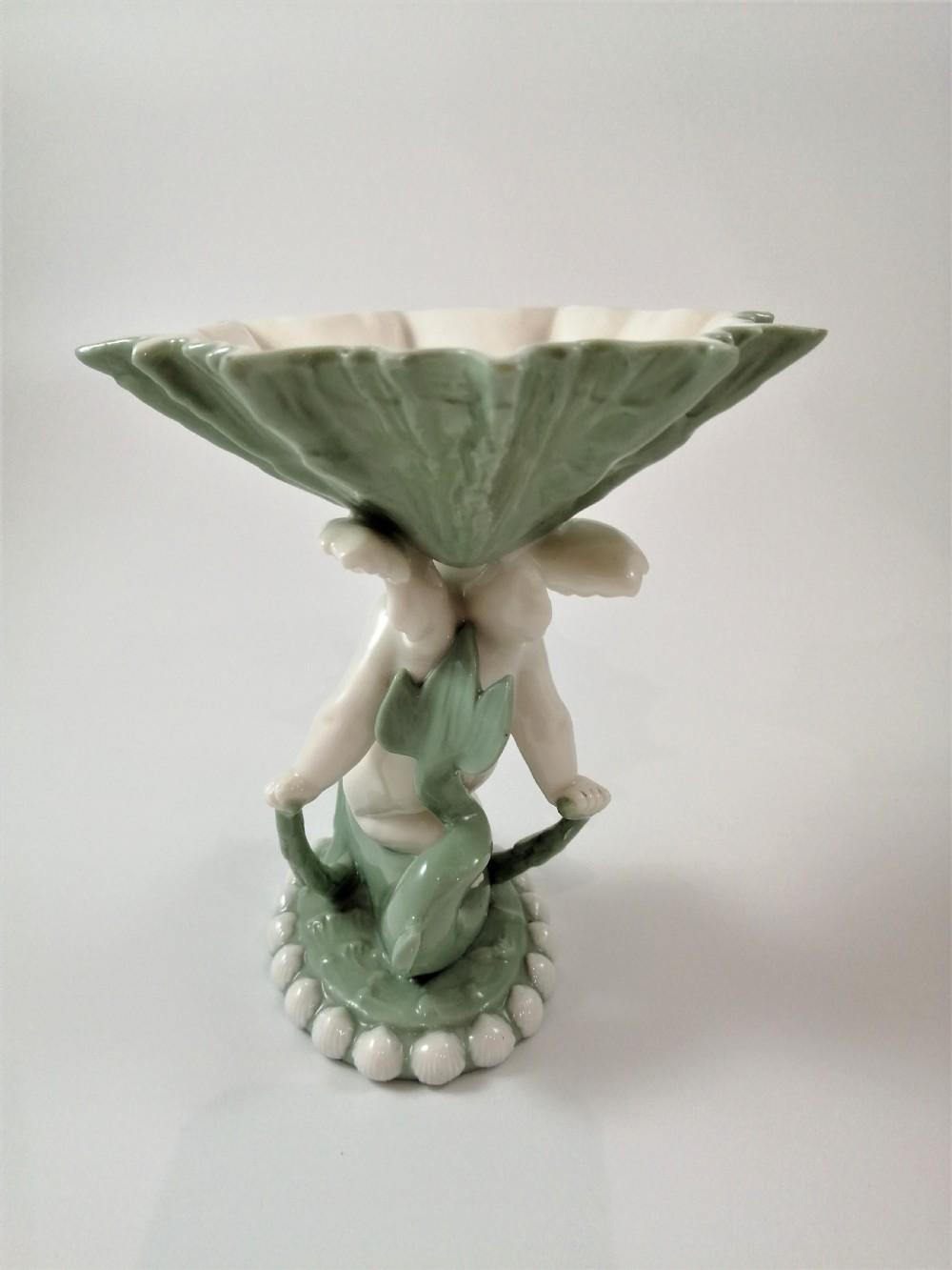 A pair of Victorian ceramic compotes featuring unglazed white cherub figures holding green leaf-shaped bowls aloft while seated on green glazed dolphin bases. View XXI
